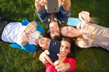 Junge Leute liegen mit Smartphone auf der Wiese