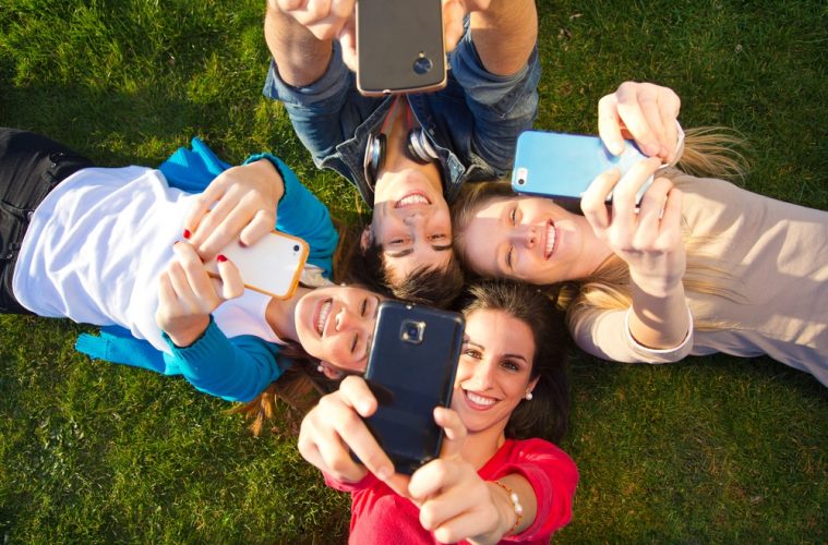 Junge Leute liegen mit Smartphone auf der Wiese
