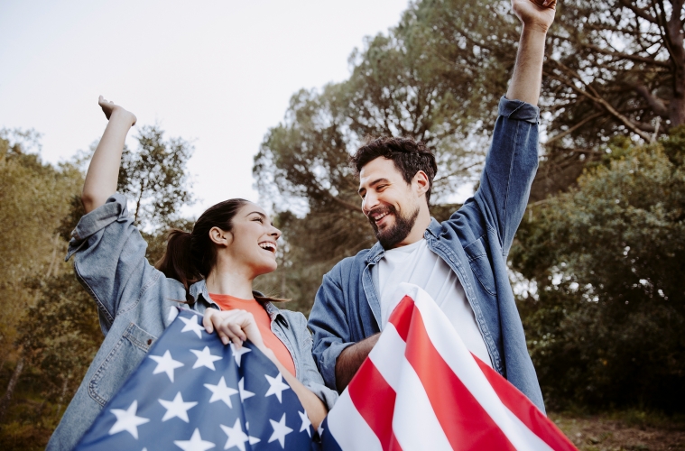 Junge Frau und junger Mann mit US-Flagge strecken die Arme in die Luft.