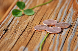 Auf einem Holztisch liegen ein Kleeblatt und 4 kupferne Münzen in Form eines Kleeblatts