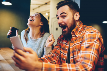 Aufgeregte männliche und weibliche Hipster freuen sich über den Gewinn einer Internet-Lotterie Wetten auf der Website auf modernes Smartphone.Glückliches Paar in Liebe feiern Sieg in Online-Wettkämpfen genießen Erfolg